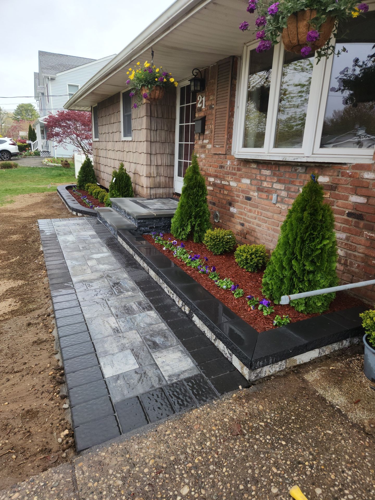Front of brick house with new stone walkway and landscaped garden bed with small trees and flowers.