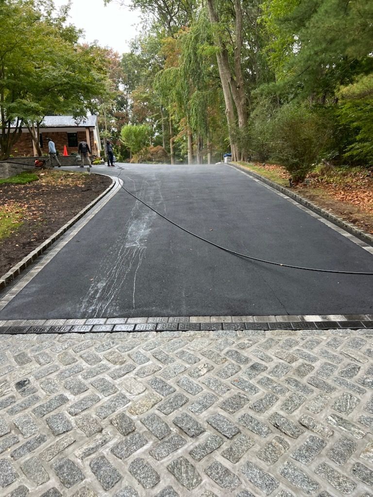 Freshly paved driveway surrounded by trees, with workers visible in the distance.