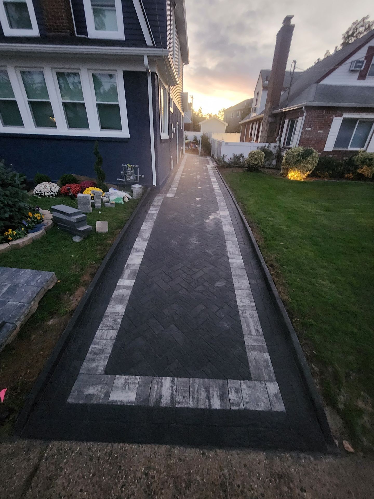Narrow paved pathway between two houses with a sunset in the background.
